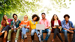 culturally diverse group of millennials sitting outside with laptops
